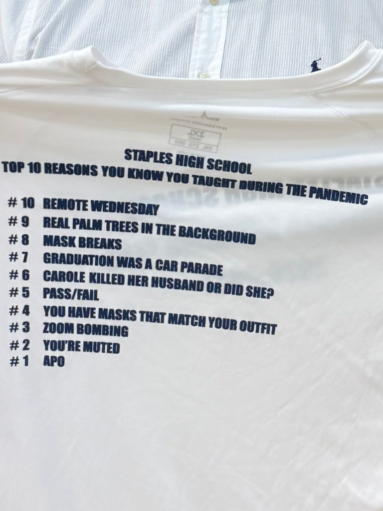 The principal proudly holding up a t-shirt from the pandemic years.